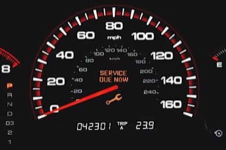 A gauge cluster with an orange wrench warning light labeled 'Service Due Now'