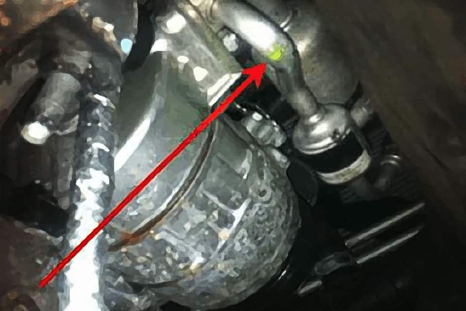Red arrow pointing to a green dot of fluid leaking out of a condensor