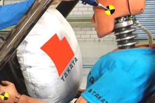 A crash test dummy about to hit an airbag with the Takata logo superimposed on top.