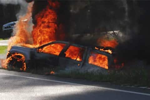 A Jeep on fire on the side of the road
