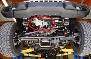 A red circle highlights the sway bar disconnect system on the bottom front of a Jeep hoisted up on lifts.