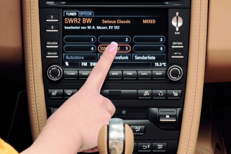 A hand pressing the touchscreen interface of Porsche's PCM infotainment system