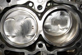 A close-up of a clean black head gasket above two silver pistons.