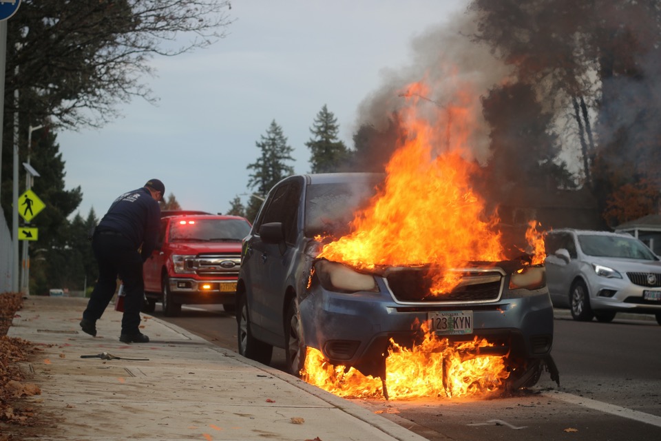 Emergency workers near a car with its engine on fire