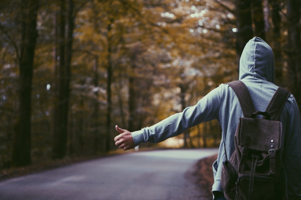 A hitchhiker on the side of the road with their thumb out