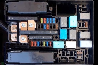 An overhead view of a car's fuse box with various colored fuses