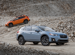 A dirt track with a blue Crosstrek in the foreground, orange Crosstrek in the background