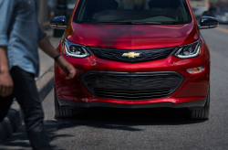 A red Chevy Bolt at a crosswalk while a pedestrian passes