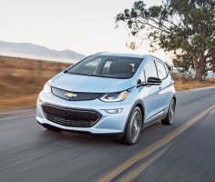 A light blue Chevy Bolt driving on a country road