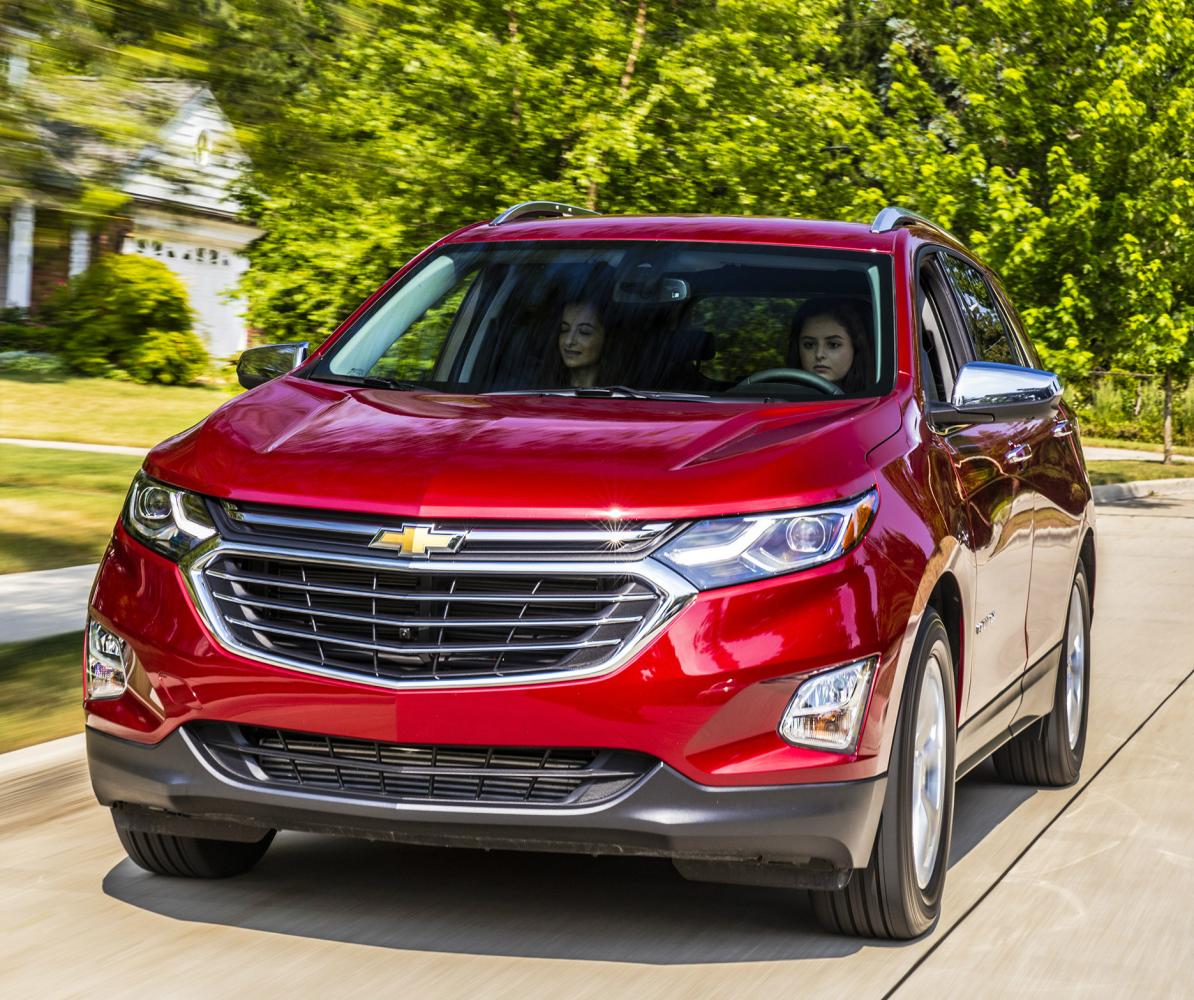 Two young woman driving a red Chevy Equinox with blurred green trees in the background