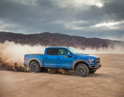 A blue F-150 is riding through a flat, sandy area with a plume of dust behind it