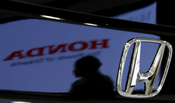 A person silhouette and the Honda logo are reflected in a car's paint