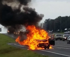 A car engulfed in flames on the side of the road