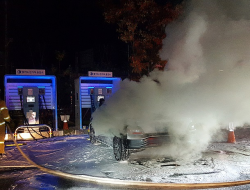 Smoke billows out of a car in front of some EV chargers