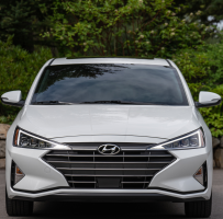 Front view of a white Hyundai parked in front of some greenery