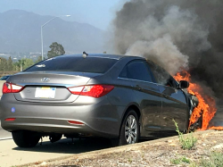 Hyundai sedan on the side of the road with the engine compartment in flames and thick smoke.