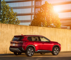 A red Rogue in front of a fence with the sun reflecting in a background building