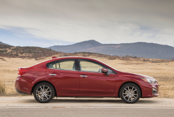 Side view of a red Subaru sedan on a dusty desert road.